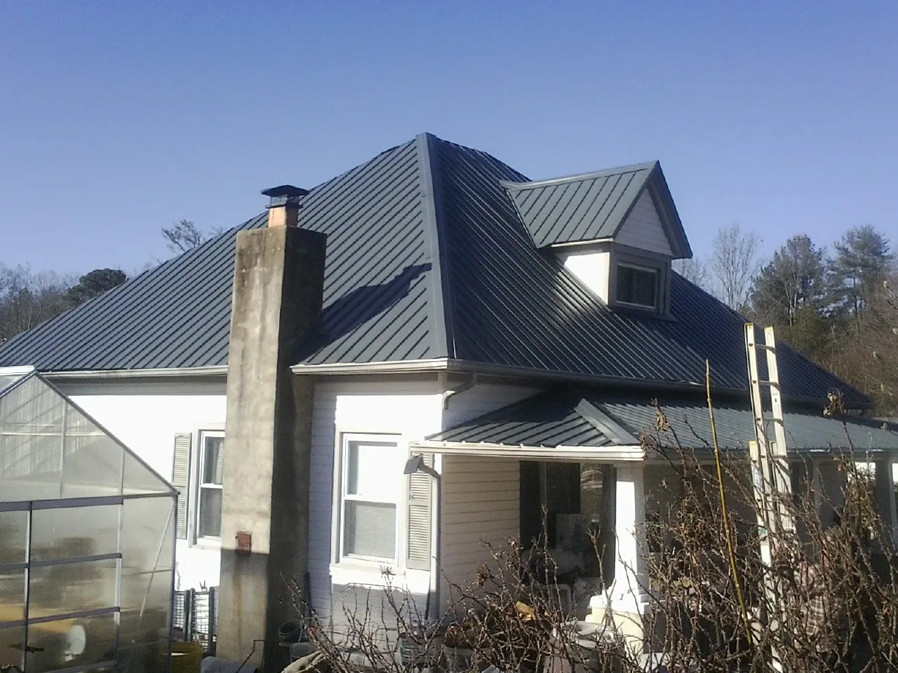 Dark blue standing seam metal roof on a white farmhouse with dormer — Slate & Tile Roof Repair by Roofing Brothers in Eleva