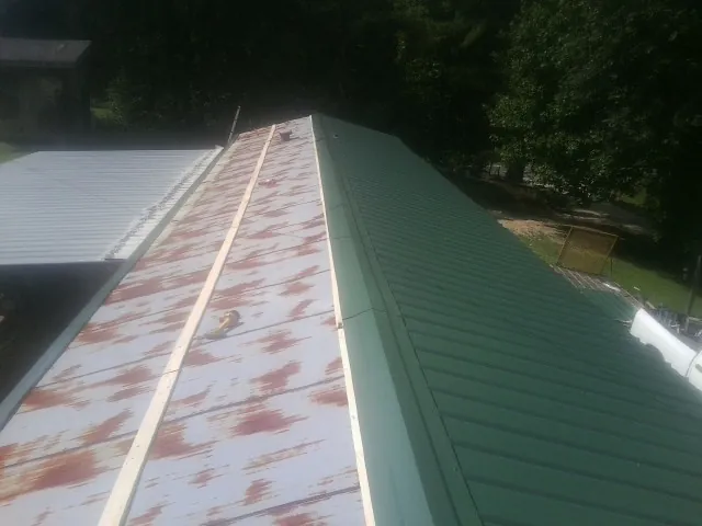 Old rusted panels beside newly installed green metal roofing — Wind Damage Roof Repair by Roofing Brothers in Eleva
