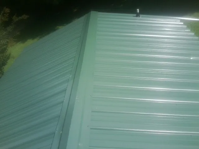 New green metal panels meeting at the ridge of a roof — Flat Roof Repair work by our crew in Eleva