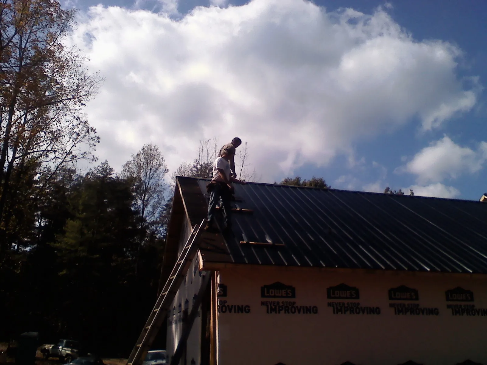 Roofer fastening dark metal panels high against a cloudy sky, from a Roof Inspection job in Eleva