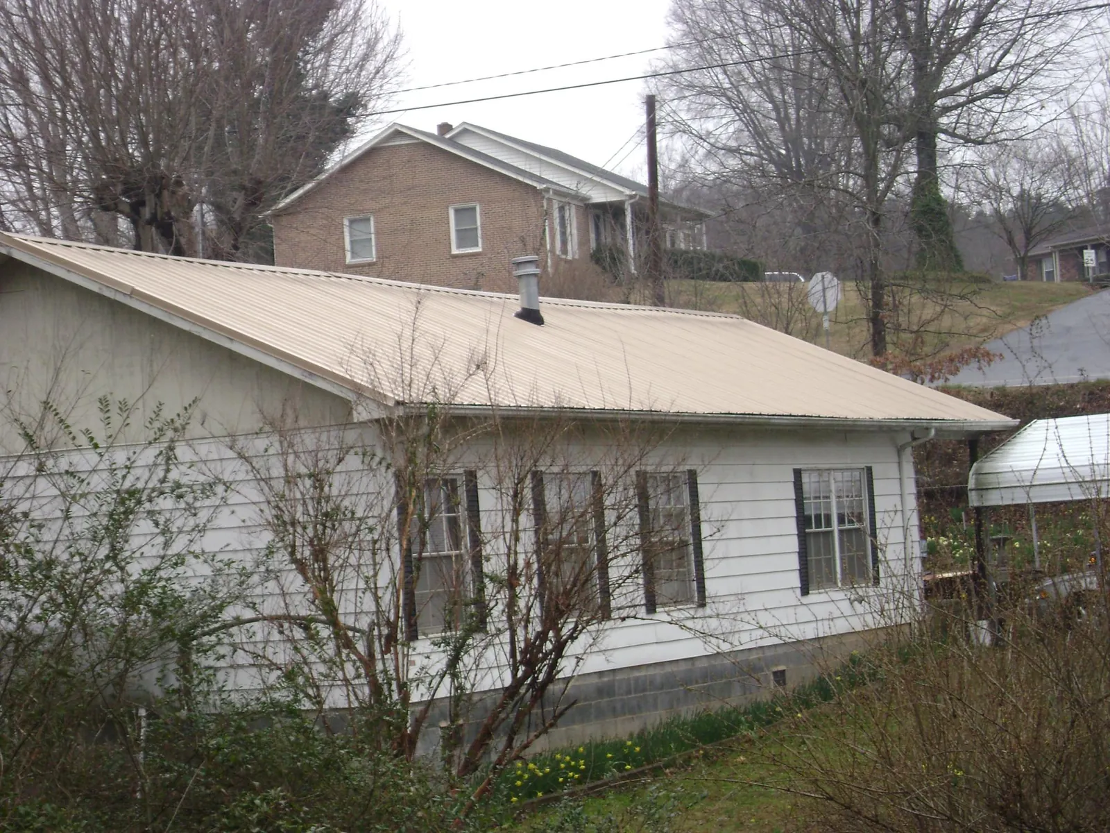 Tan metal roof on a white sided house set into a hillside — Commercial Roofing by Roofing Brothers in Eleva