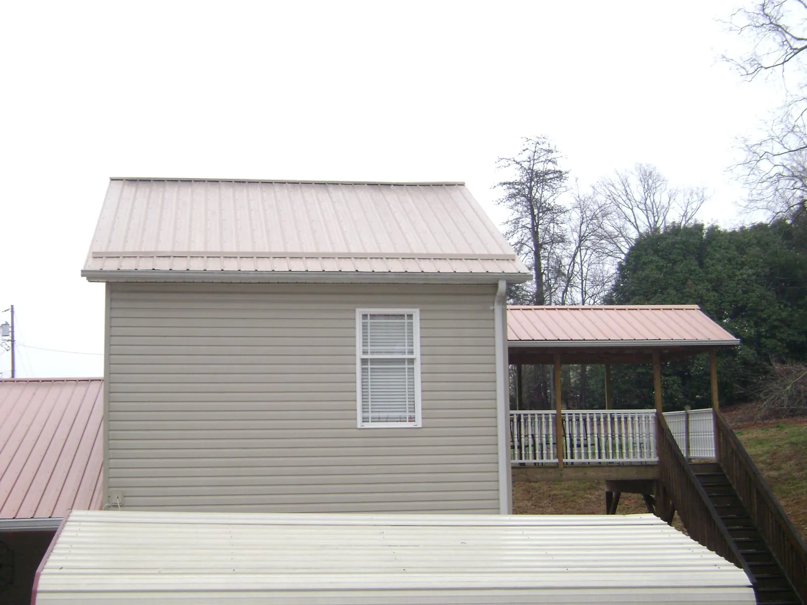 Tan metal roofs on a two story addition and attached porch, from a Roof Replacement job in Eleva
