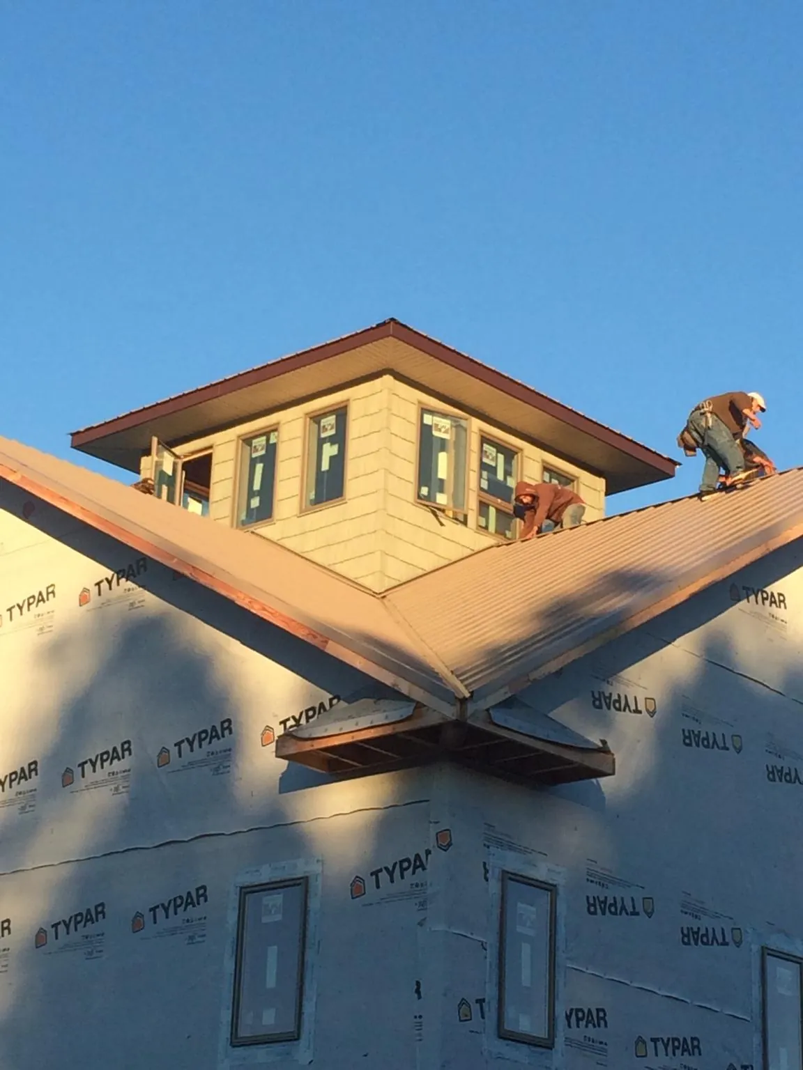 Roofers working around a rooftop cupola on a new metal roof at sunset — Roof Waterproofing in Eleva by Roofing Brothers